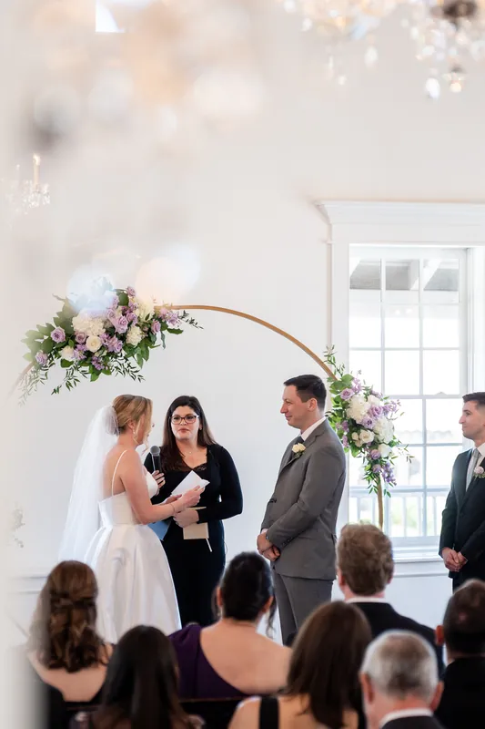 Sarah and Tim kiss under the wooden floral arch as their officiant smiles nearby.