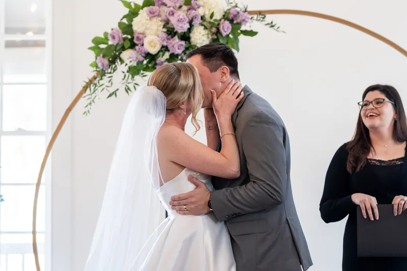 Sarah and Tim embrace after their first kiss, with their officiant beaming alongside them.