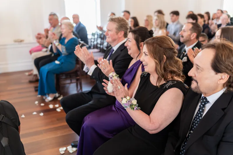 Wedding guests seated in rows clap and smile as the couple celebrates their union.