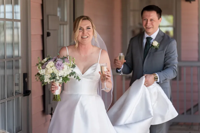 Sarah smiles broadly while holding her bouquet as Tim walks beside her in their receiving line.