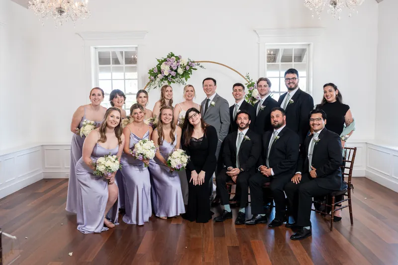 Sarah and Tim stand centered with their full wedding party—twelve attendants in coordinating lavender and black—in front