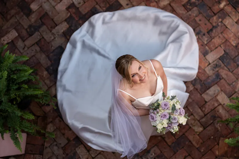 Overhead view of Sarah lying on a brick floor in her white dress and veil, holding her bouquet.