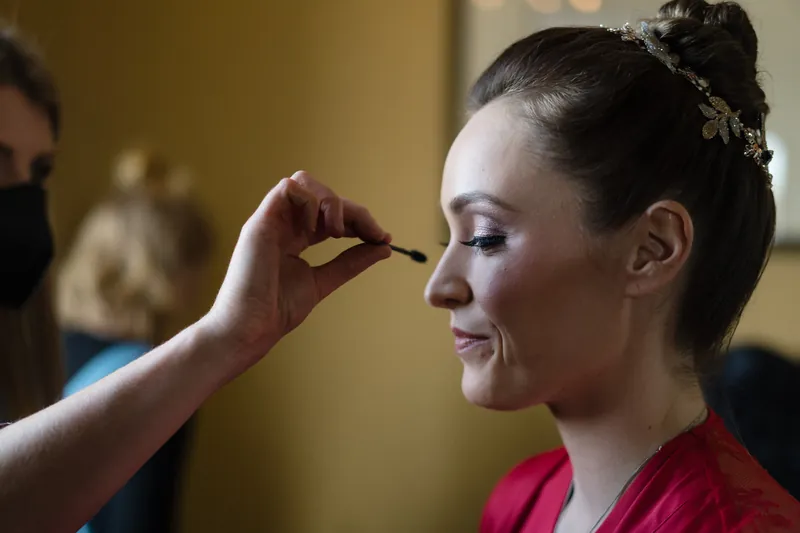 Simone's eyes close as a makeup artist applies eyeshadow during bridal preparation.