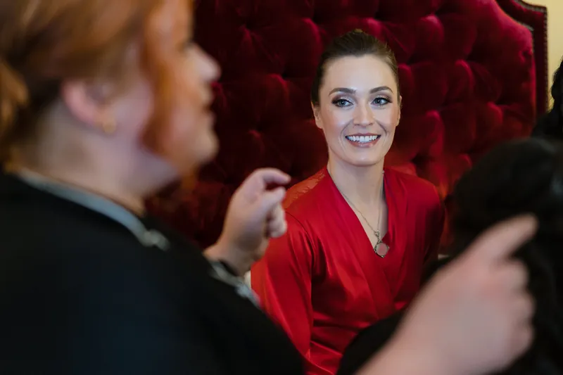 Simone laughs with attendants in a red robe against a deep crimson velvet backdrop.
