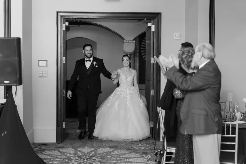 Michael and Simone emerge from an indoor doorway as guests wave in welcome at the reception.