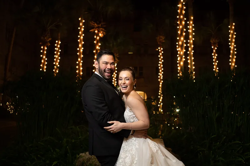 Simone and Michael embrace outdoors surrounded by illuminated trees and dark foliage.