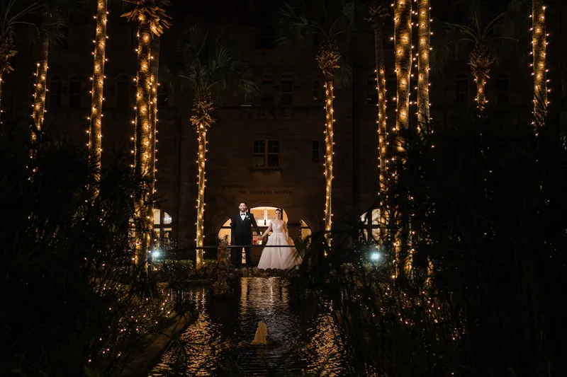 The couple walks together down a lit courtyard lined with glowing palm trees at the resort.