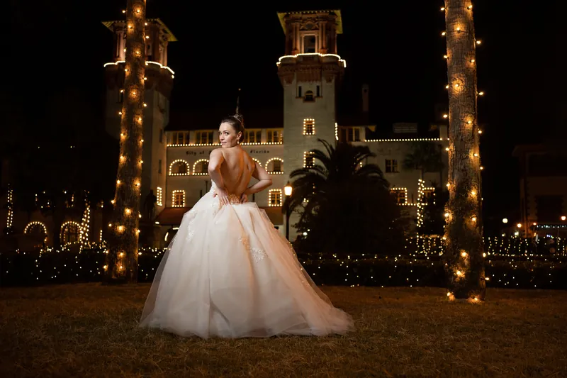 Simone stands alone in her ballgown on the grounds, the historic resort building glowing behind her.