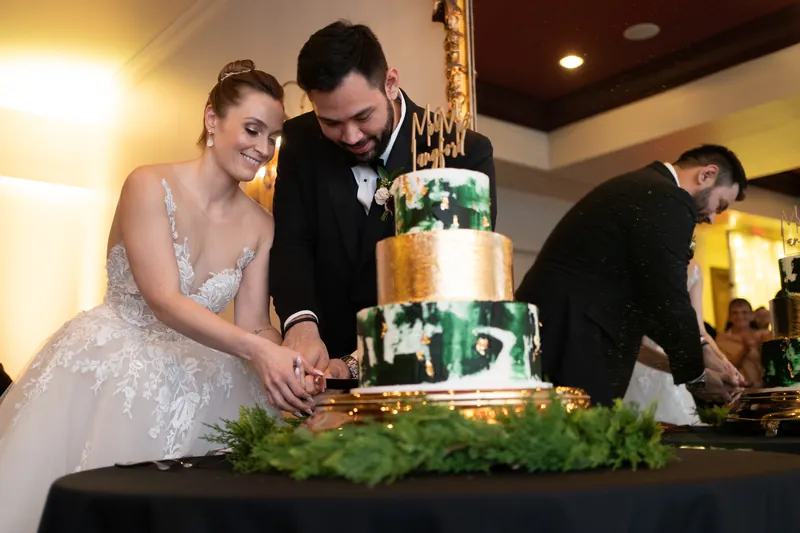 Simone and Michael place their hands together on a tiered cake with green floral accents.