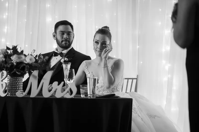 Michael and Simone sit at their sweetheart table with a "Mr & Mrs" sign and flowers.