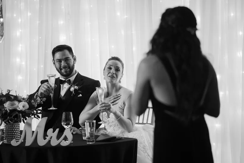 A guest approaches the reception table to speak with Michael and Simone as they sit together under the illuminated backdrop.