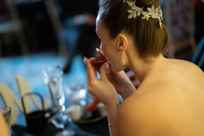 Simone pauses thoughtfully, hand near her face, wearing a gold leaf hairpiece at the reception.