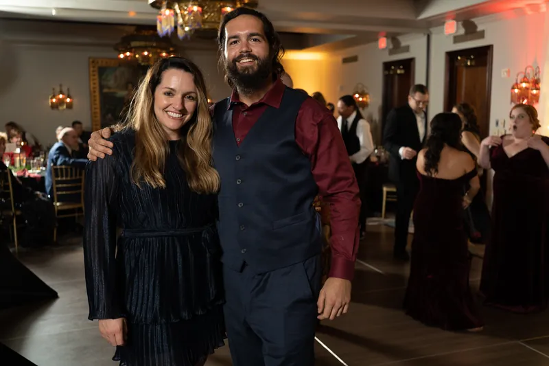 A guest poses with Michael at the reception, both smiling warmly in the warmly lit venue.