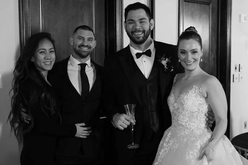 Simone in her lace gown stands with Michael and two other guests in a black and white portrait.