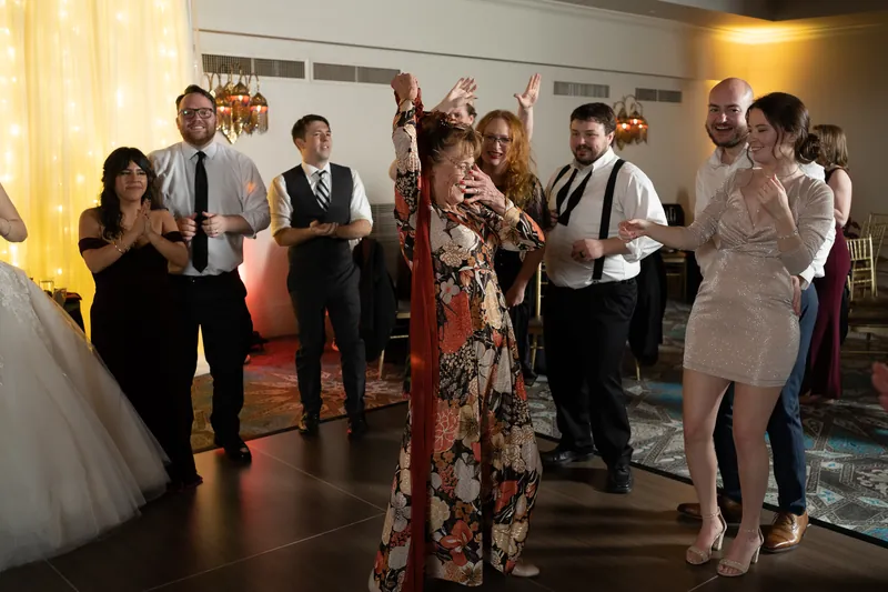 Wedding guests dance and celebrate on the ballroom floor with golden curtain lighting behind them.