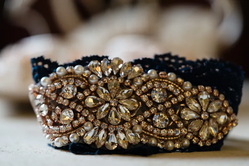 A black velvet belt features an ornate gold and crystal floral buckle, displayed on a neutral surface.