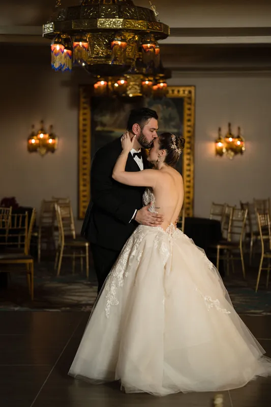 The couple embraces during their first dance beneath elegant gold-trimmed mirrors and sconces.
