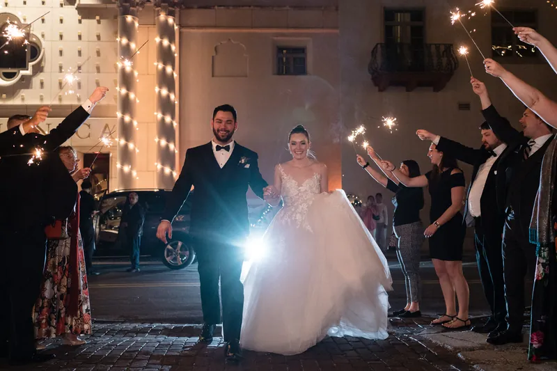 Simone and Michael walk through a sparkler exit as guests line both sides with lit sparklers overhead.