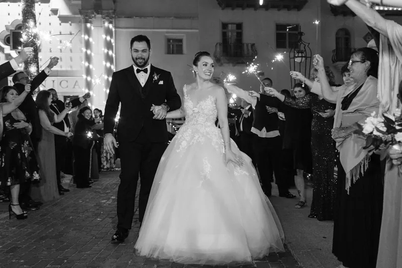Simone and Michael walk hand-in-hand down the guest-lined courtyard at Casa Monica, formal attire catching the evening light.
