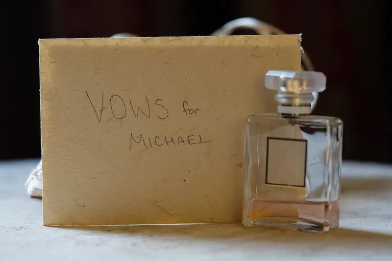 Handwritten vows addressed to Michael rest beside a square glass perfume bottle on a cream envelope.