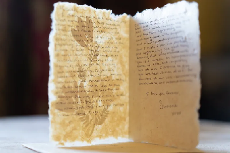 An open booklet displays handwritten text and gold watercolor designs across both facing pages.