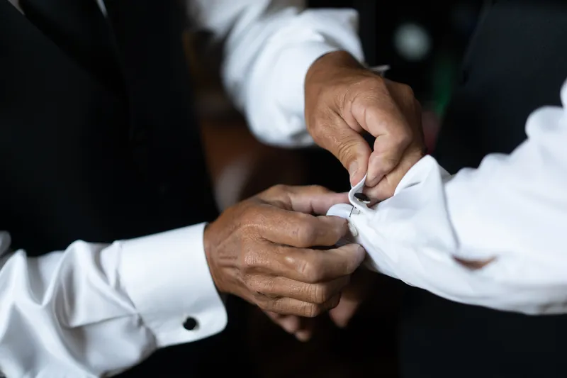 Two people in white dress shirts clasp hands together in a close-up moment.