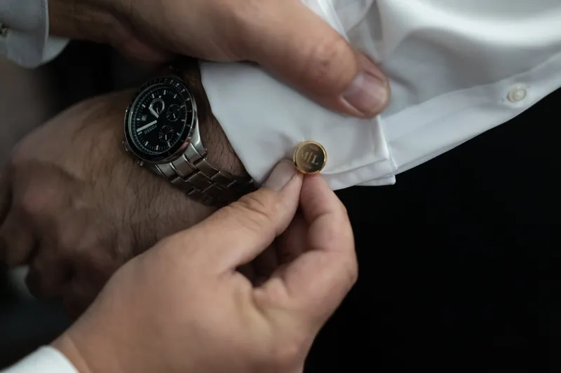 Michael's hand displays a cufflink while Simone holds it near his wrist wearing a dark watch.