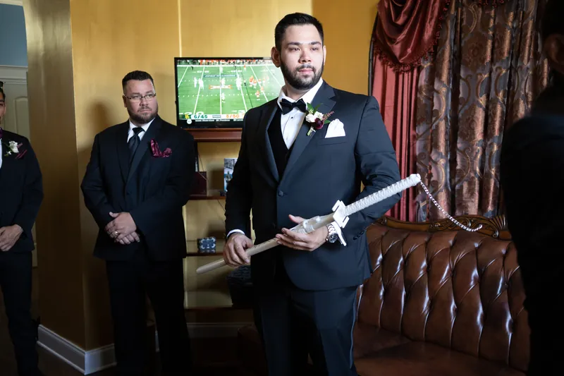 Michael holds a rolled document in a black tuxedo with boutonniere, flanked by groomsmen in formal attire.