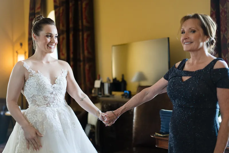 Simone in her ivory beaded gown holds hands with a woman in a black sleeveless dress, both smiling warmly.