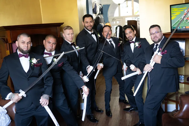 Michael and six attendants hold decorative swords with white ribbons in a yellow-walled room.