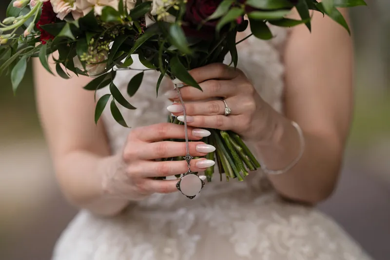 Simone's hands hold a bouquet of roses and eucalyptus while displaying her diamond engagement and wedding rings.