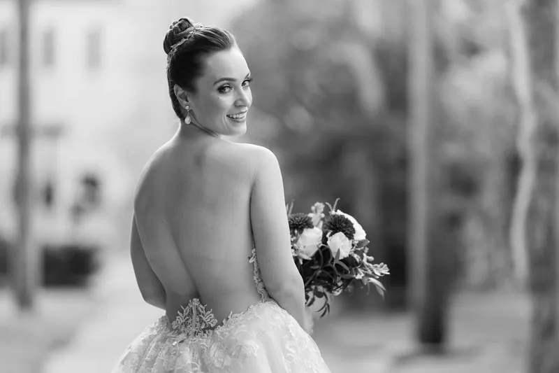 Simone looks over her shoulder in a low-back beaded gown, clutching her bouquet in black and white photography.