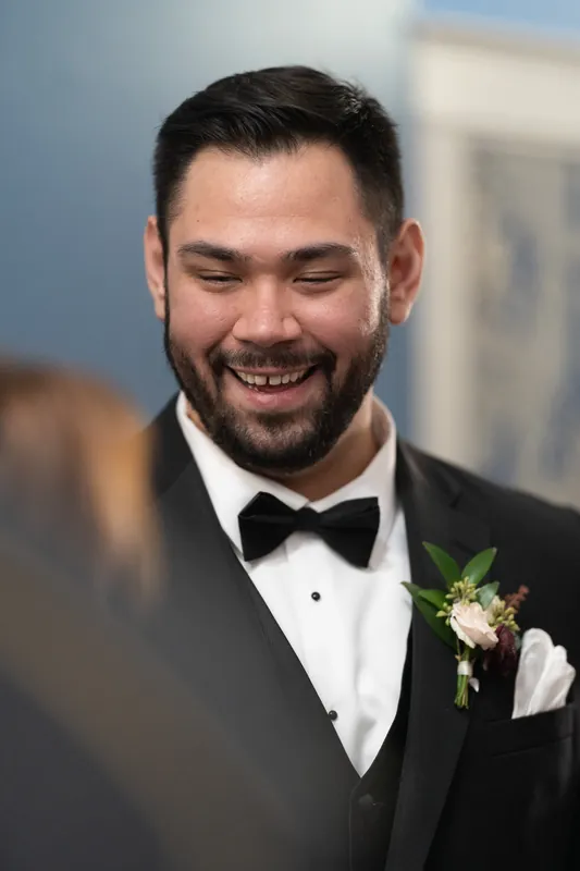 Michael smiles broadly in a black tuxedo with bow tie and white boutonniere at Casa Monica Resort & Spa.