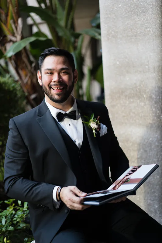 Michael holds an open program while seated, wearing a dark suit jacket and boutonniere.
