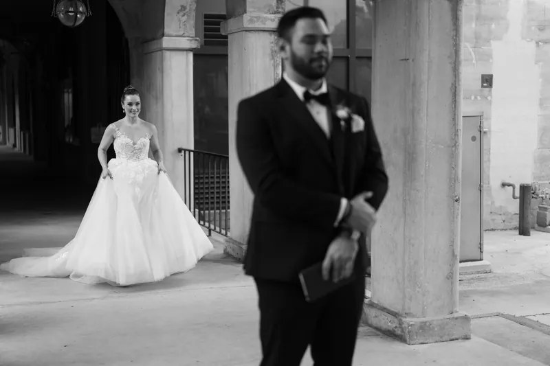 Michael stands in formal black attire as Simone approaches in her white wedding gown through the archway.