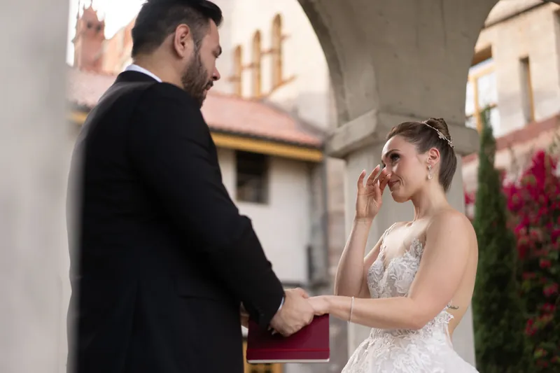 Simone touches her face with a bright smile while Michael holds her hand in front of the Spanish colonial courtyard.