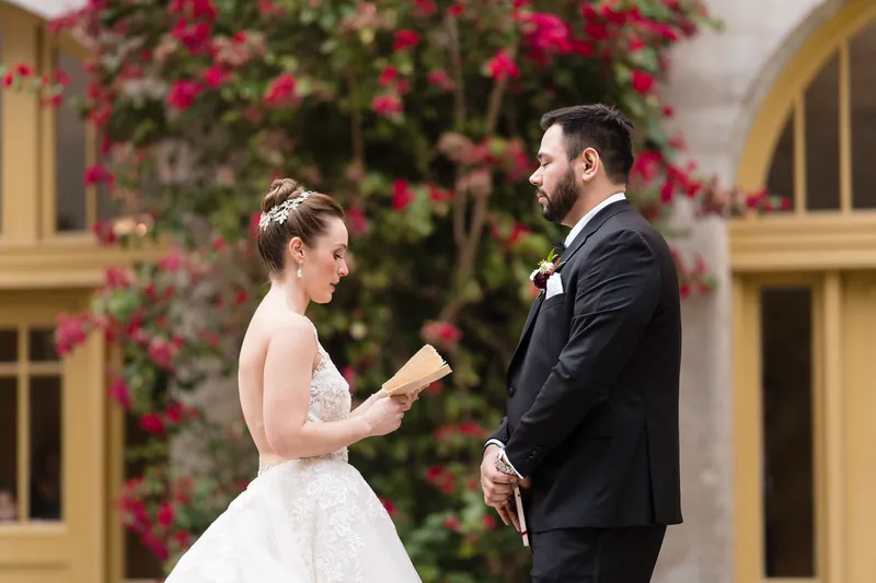 Simone holds a handwritten note while facing Michael beneath blooming magenta flowers and golden archways at Casa Monica.