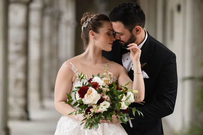 Michael kisses Simone's cheek as she holds a burgundy and cream bouquet under Casa Monica's arched corridor.