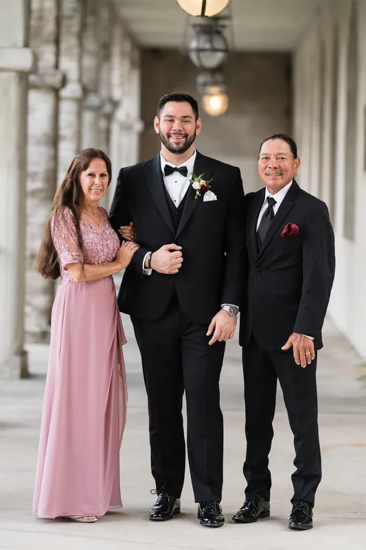 Michael stands between two family members in formal attire along the columned walkway at Casa Monica Resort & Spa.
