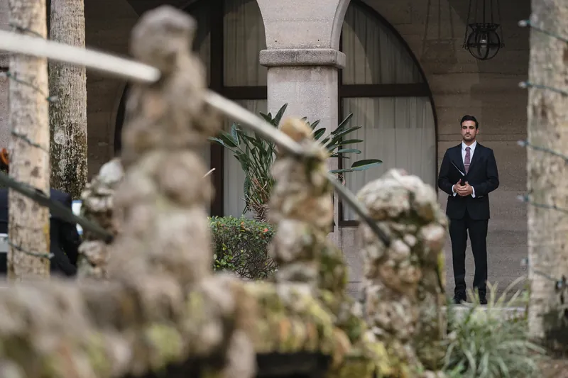 Michael stands in a dark suit among flowering plants in the Casa Monica Resort & Spa courtyard.