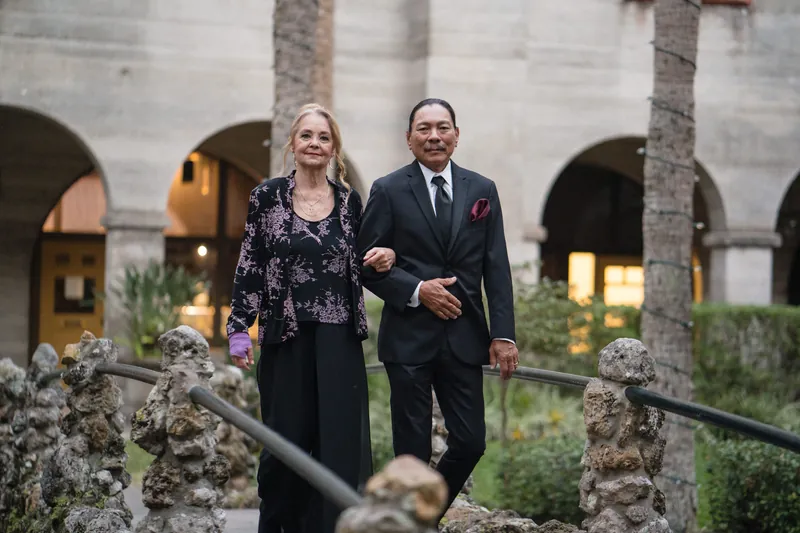 Simone and Michael walk arm-in-arm through the arched colonnades lined with palm trees at Casa Monica.