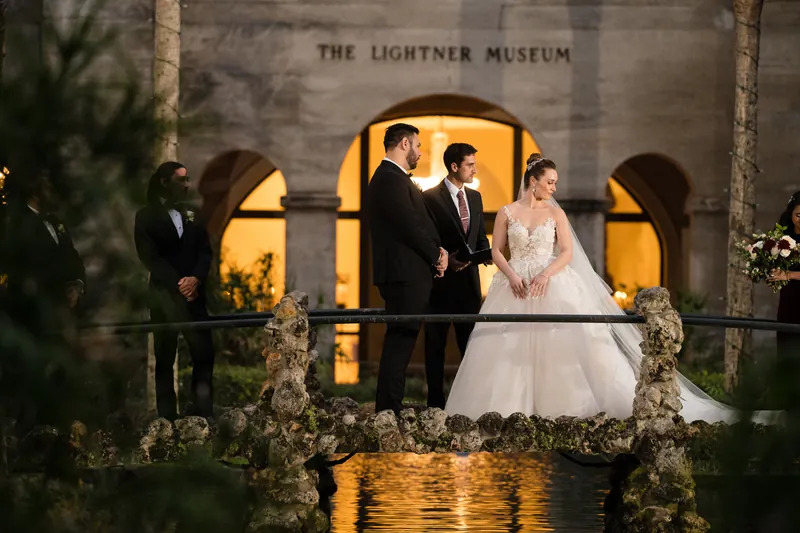 Michael and Simone stand on an illuminated balcony framed by glowing archways with wedding guests nearby.