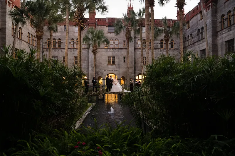 Simone and Michael pose in the courtyard surrounded by palms and Spanish colonial architecture at dusk.