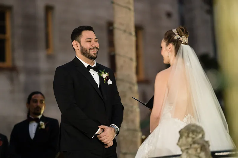 Michael gazes at Simone as she holds her bouquet during their ceremony, with groomsmen visible in the background.