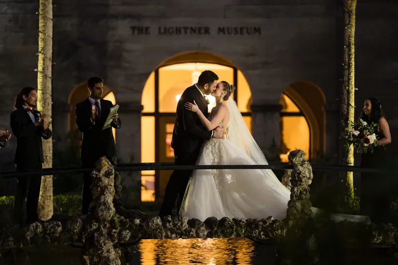 Michael and Simone kiss on the lit balcony at Casa Monica Resort & Spa, with guests and foliage flanking the moment.