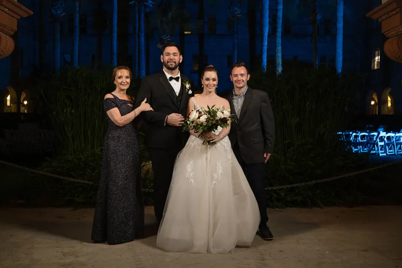 Michael and Simone pose with two family members in formal attire, Simone holding her bouquet under the resort's lit archway.