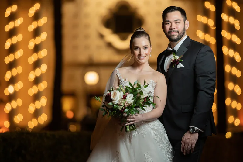 Simone and Michael pose together with warm golden light from decorative panels framing them at the venue.