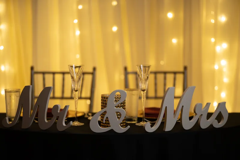 Decorative "Mr & Mrs" lettering glows against draped fabric and ambient light at their reception.