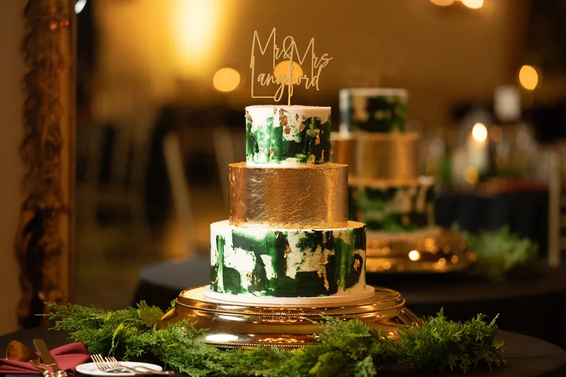 A two-tiered wedding cake decorated with greenery and topped with a "Mr & Mrs" cake topper sits on moss.