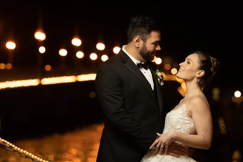 Michael and Simone embrace outdoors at night, with string lights glowing softly in the background.